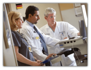 doctors and technicians looking at laptop in patient room